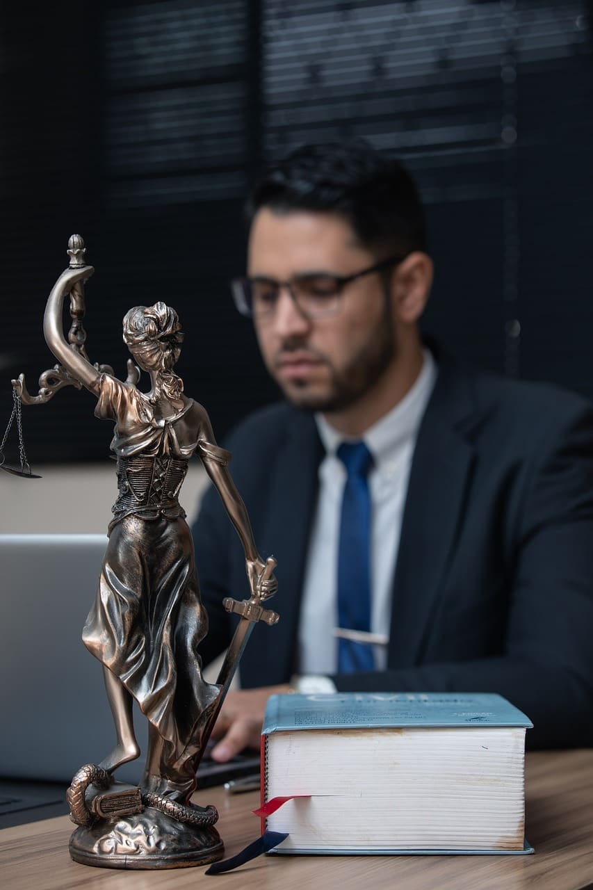 An attorney working at a desk with a statue of Lady Justice and a law book in the foreground, representing intellectual property counsel for Joplin, Missouri